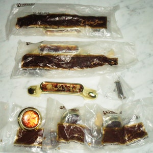 Puede incluir: Un juego de seis pomos de armario dorados con un inserto de vidrio decorativo. Los pomos están empaquetados en bolsas de plástico transparentes con el logotipo de Amerock e información del producto.