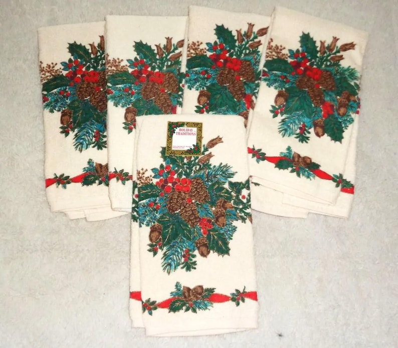 May include: Set of six off-white holiday towels. Each towel features a festive design of pinecones, holly, and red berries. A red ribbon with green accents adorns the bottom. The towels are perfect for seasonal decor.