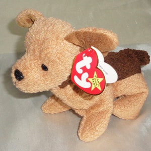 Peut inclure: Un jouet en peluche de chien brun et beige Ty Beanie Baby avec une oreille brune et une étiquette rouge qui dit "Ty Beanie Original Baby" et "style 4108".
