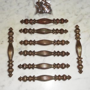 Peut inclure: Huit poignées de porte de placard en laiton antique avec des détails ornés. Les poignées ont une finition légèrement vieillie et sont en bon état.