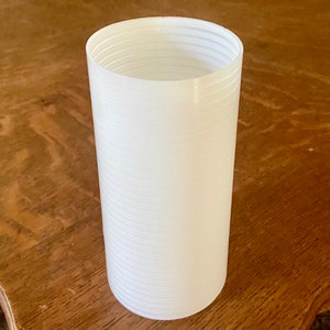 May include: A white plastic cylinder with a ribbed texture. The cylinder is empty and appears to be a container.
