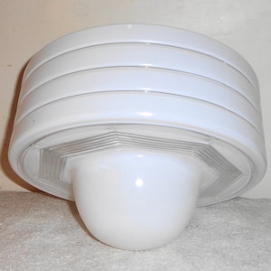 May include: White ceiling light fixture with a rounded, layered design. The fixture has a white, opaque glass shade with a textured, geometric pattern.