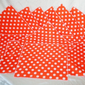 Pu&ograve; includere: Un set di tovaglioli di stoffa arancioni con un motivo a pois bianchi. I tovaglioli sono disposti a ventaglio, mettendo in risalto il loro colore vivace e il loro design giocoso. Il tessuto sembra essere cotone o un materiale simile.