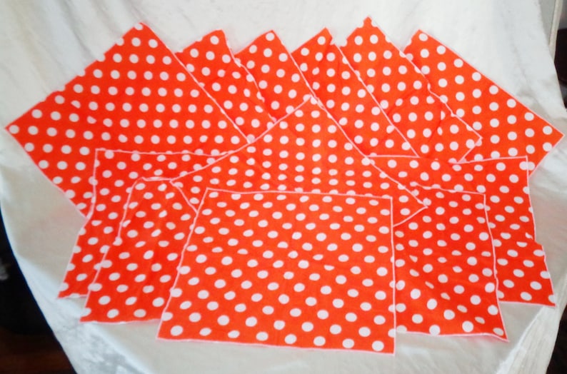 Pu&ograve; includere: Un set di tovaglioli di stoffa arancioni con un motivo a pois bianchi. I tovaglioli sono disposti a ventaglio, mettendo in risalto il loro colore vivace e il loro design giocoso. Il tessuto sembra essere cotone o un materiale simile.