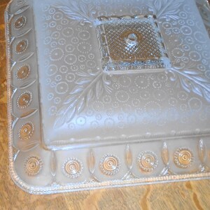 May include: A frosted glass ceiling light fixture with a square shape and a decorative design. The fixture has a central opening for a light bulb and a raised, textured border.