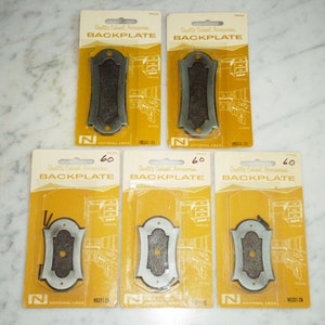 Könnte beinhalten: Fünf Verpackungen mit Schrank-Rückwänden, jede mit einem anderen Design. Die Rückwände sind aus Metall und haben eine gebürstete Nickel-Oberfläche. Die Verpackungen sind mit "Quality Cabinet Accessories" und "Backplate" beschriftet.