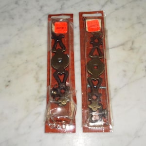 May include: Two packages of brass drawer pulls with ornate designs. The packages are labeled "Lampert's Imports".
