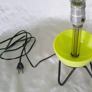 May include: A yellow ceramic lamp base with a black wire and plug. The lamp has a metal stand with three legs and a clear glass globe on top.