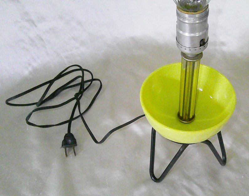 May include: A yellow ceramic lamp base with a black wire and plug. The lamp has a metal stand with three legs and a clear glass globe on top.