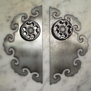 Può includere: Un paio di maniglie per porte argentate con intricati disegni a spirale. Ogni maniglia presenta un pomo decorativo circolare con un motivo floreale.