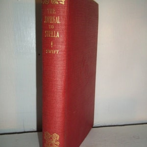 Könnte beinhalten: Ein rotes Hardcover-Buch mit dem Titel "The Journal to Stella" von Swift. Der Buchrücken weist goldene Schrift und dekorative Akzente auf. Auf dem unteren Buchrücken steht "Bohn's Popular Library".