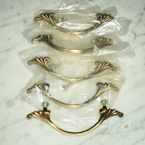 May include: Four gold-toned cabinet door pulls with a decorative, ornate, fan-shaped design. The pulls are packaged in clear plastic bags.