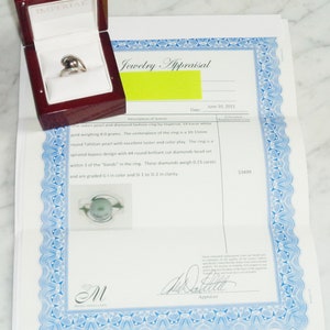 Pode incluir: Um certificado de avalia&ccedil;&atilde;o de joias para um anel de p&eacute;rola e diamantes. O certificado &eacute; datado de 10 de junho de 2013 e declara que o anel &eacute; de ouro branco de 18 quilates, pesa 8,0 gramas e apresenta uma p&eacute;rola redonda do Taiti de 10-11 mm. O anel tamb&eacute;m tem 44 diamantes de corte brilhante redondo que pesam 0,23 quilates. O valor da avalia&ccedil;&atilde;o &eacute; de 3499 &euro;.
