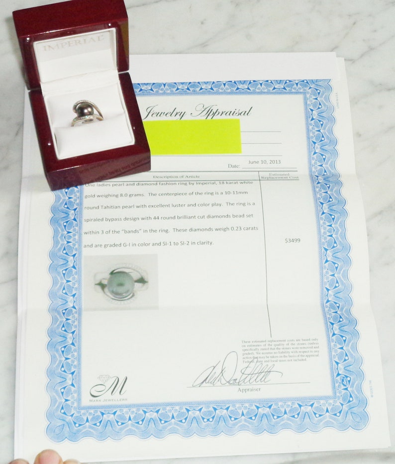 Pode incluir: Um certificado de avalia&ccedil;&atilde;o de joias para um anel de p&eacute;rola e diamantes. O certificado &eacute; datado de 10 de junho de 2013 e declara que o anel &eacute; de ouro branco de 18 quilates, pesa 8,0 gramas e apresenta uma p&eacute;rola redonda do Taiti de 10-11 mm. O anel tamb&eacute;m tem 44 diamantes de corte brilhante redondo que pesam 0,23 quilates. O valor da avalia&ccedil;&atilde;o &eacute; de 3499 &euro;.