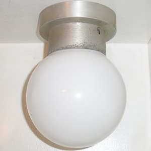 Puede incluir: Una lámpara de globo blanco con una base de metal plateado.