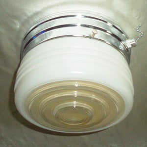 May include: A white ceiling light fixture with a chrome finish and a pull chain. The light has a frosted glass shade with a layered design.