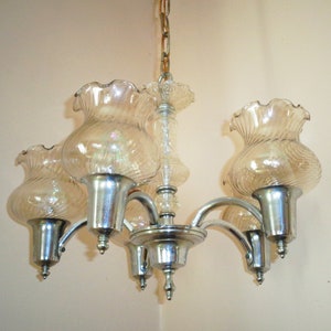 May include: A chrome chandelier with five clear glass shades. The shades have a ruffled edge and a textured pattern.