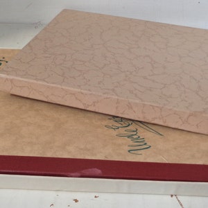 May include: A closed book with a red spine and a white slipcase. The book cover is brown with the text "Howdy Ev'rybuddy!" printed in green. The slipcase is also brown with a textured pattern.