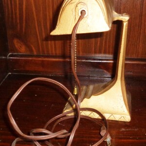 May include: A gold-colored desk lamp with a decorative design. The lamp has a brown cord and a chain hanging from the top.