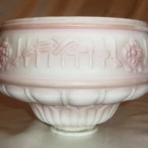 May include: A white glass lampshade with a pink rim and embossed floral design. The shade has a scalloped bottom edge.