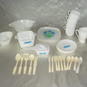 Puede incluir: Una colección de vajilla blanca vintage y utensilios para servir. Incluye platos con diseños florales azules, cuencos para servir, una jarra de crema y una pila de fuentes. También incluye un juego de cuchillos, tenedores, cucharas y cucharas para servir.