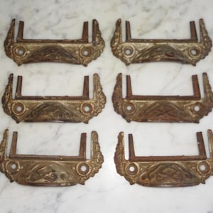 May include: Six antique drawer pulls with ornate designs. The pulls are made of metal and have a gold finish. They are in good condition with some signs of wear.