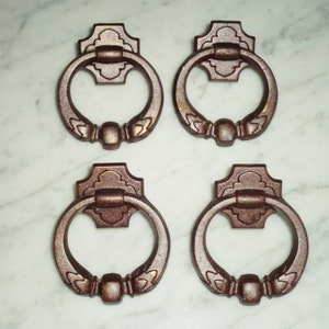 Puede incluir: Conjunto de cuatro tiradores de puerta de bronce de estilo antiguo con detalles ornamentados. Cada tirador tiene un asa de anillo y una placa posterior decorativa.