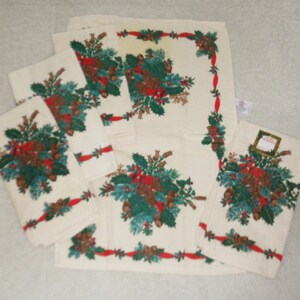 May include: A set of off-white Christmas-themed towels. Each towel features a festive design of pine cones, holly, and red ribbons. The towels are arranged in a neat stack, showcasing the holiday pattern.