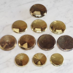 May include: Ten gold-coloured metal round discs of varying sizes. The discs have a smooth, shiny surface and a slightly raised edge.