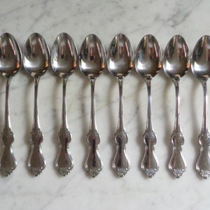 Pode incluir: Oito colheres de prata com cabos ornamentados. As colheres estão dispostas em uma fila, com os cabos voltados para o observador.