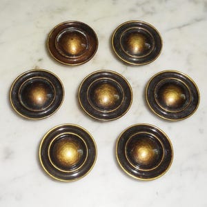 May include: Seven round, brass-coloured cabinet knobs with a raised, domed centre. The knobs have a slightly textured finish.