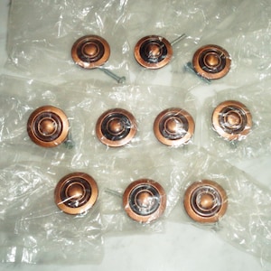 May include: Ten copper-colored round cabinet knobs with a raised center ring. The knobs are displayed on a white plastic sheet.