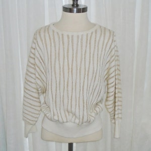 May include: A white sweater with gold stripes. The sweater is made of a soft, knit fabric and has a relaxed fit.