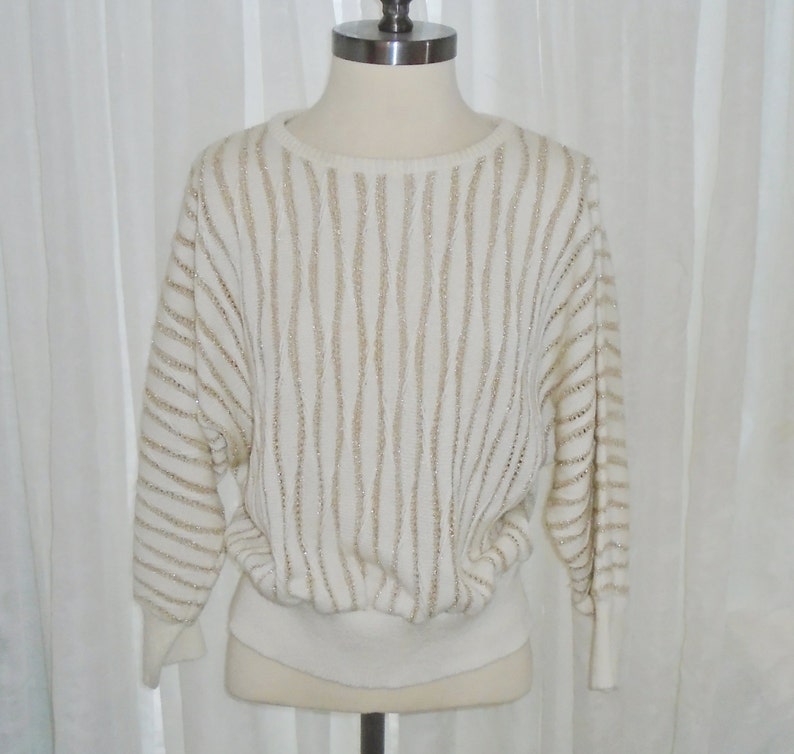 May include: A white sweater with gold stripes. The sweater is made of a soft, knit fabric and has a relaxed fit.