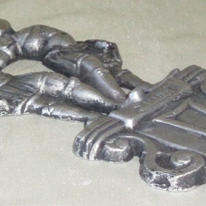Puede incluir: Una decoraci&oacute;n de pared de metal plateado con dos figuras que se toman de la mano, con la palabra "G&eacute;minis" inscrita en la base.