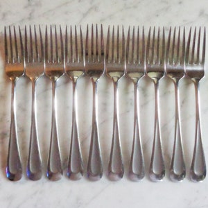 Könnte beinhalten: Ein Set mit 14 silbernen Gabeln in einem schlichten, eleganten Design. Die Gabeln sind in einer Reihe angeordnet, mit den Zinken nach oben.