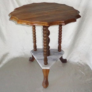 Op de afbeelding: Een houten bijzettafel met een gegolfd blad en een driehoekige marmeren plank. De tafel heeft drie poten met gedraaide spindels.