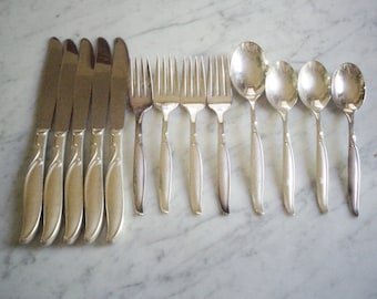 Op de afbeelding: Een set zilverkleurig bestek, waaronder messen, vorken en lepels, gerangschikt op een marmeren oppervlak. De messen hebben een gebogen handvatontwerp, terwijl de vorken en lepels een eenvoudige, elegante vorm hebben. De set is geschikt voor een formeel diner.