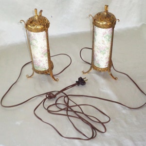 May include: A pair of gold-colored table lamps with floral patterned shades and a brown electrical cord.