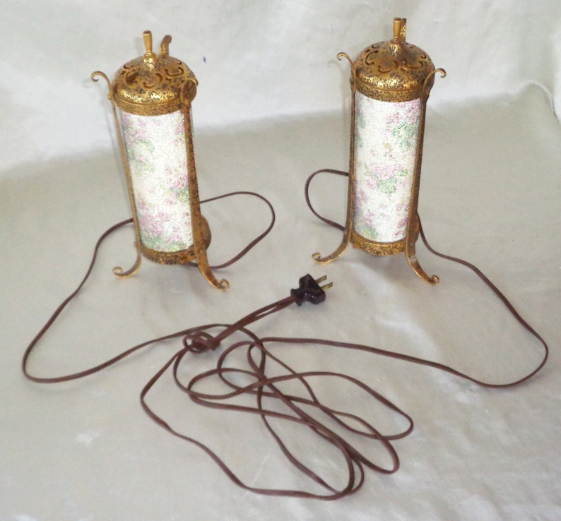 May include: A pair of gold-colored table lamps with floral patterned shades and a brown electrical cord.