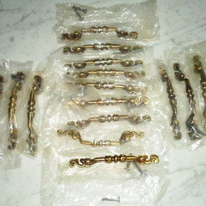 May include: A collection of 18 gold-toned cabinet door pulls with ornate designs. The pulls are packaged in clear plastic bags and include screws for installation.