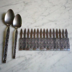 May include: A set of 18 silver-toned, ornate, decorative, metal,  spoons with a decorative, floral design. The spoons are arranged in a row, with the handles facing up.