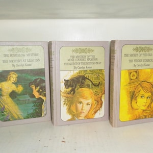 May include: Three vintage hardcover books with light purple covers. The titles include "The Bungalow Mystery," "The Mystery at Lilac Inn," "The Mystery of the Moss-Covered Mansion," "The Quest of the Missing Map," and "The Secret of the Old Clock." Each book features illustrations and the author's name, Carolyn Keene.