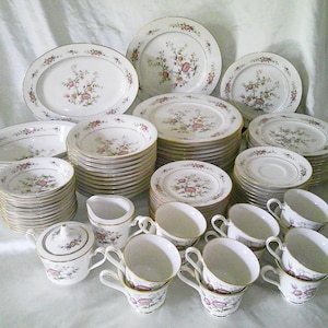 Può includere: Un grande set di stoviglie in porcellana bianca con un motivo floreale in tonalità rosa, viola e verde. Il set comprende piatti, ciotole, tazze, piattini, un bricco per la panna e una zuccheriera.