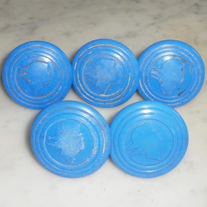 May include: Five blue plastic drawer knobs with a raised profile and a silhouette of a person's head in the center.