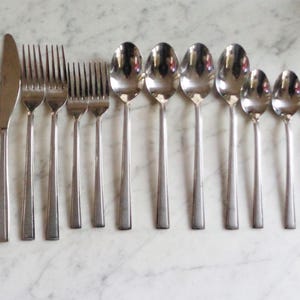 May include: A set of stainless steel silverware, including knives, forks, and spoons, arranged on a marble surface. The silverware has a simple, elegant design, with a polished finish. The set includes 2 knives, 3 forks, and 7 spoons.