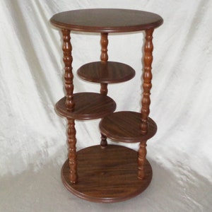 Pode incluir: Um suporte de madeira de cor castanho escuro com quatro prateleiras redondas e pernas torneadas. O suporte tem aproximadamente 61 cm de altura.