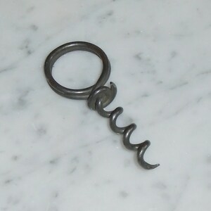 May include: A silver metal corkscrew with a ring handle.