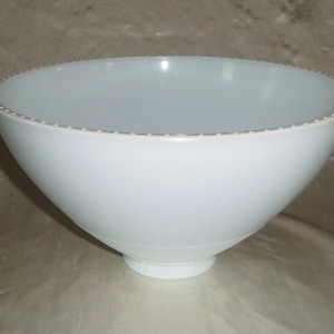 May include: A pale blue ceramic bowl with a wide, rounded shape. The rim has a delicate, dotted pattern. The bowl sits on a small, circular base, suitable for serving or display.