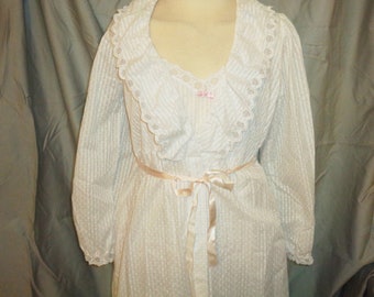 May include: White cotton nightgown with a lace trim collar and a satin ribbon tie. The gown has a dotted pattern and long sleeves.